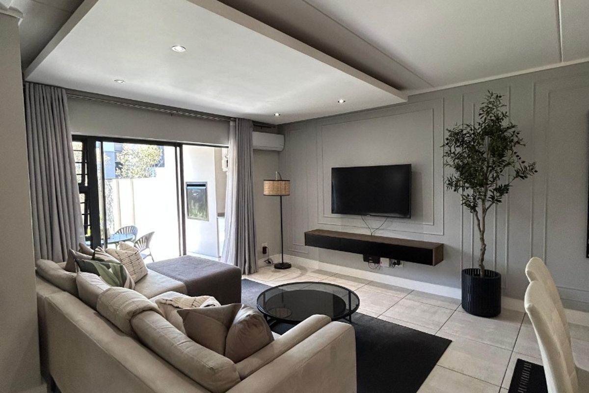 Modern living room featuring elegant wall paneling, a floating media console, recessed ceiling lighting, and large sliding doors leading to an outdoor patio area.