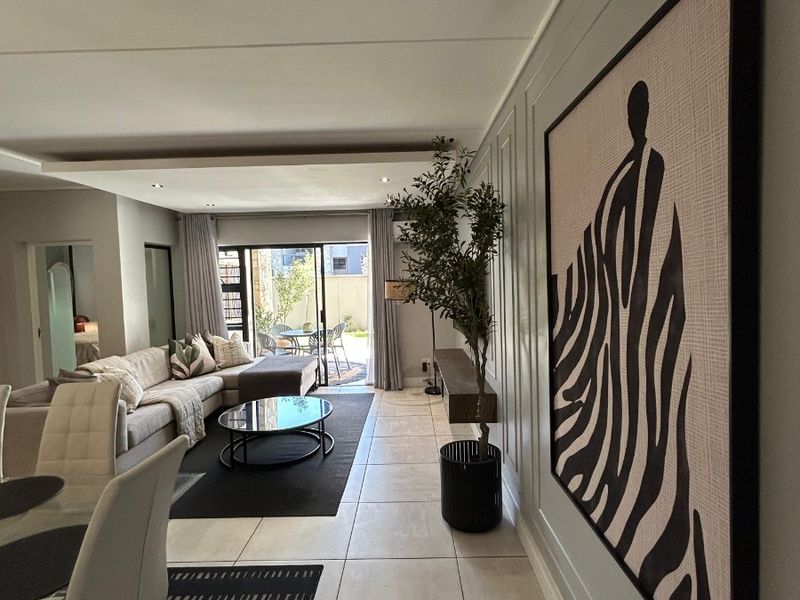 Spacious open-plan living and dining area featuring neutral tiled flooring, recessed lighting, and large sliding glass doors leading to an outdoor patio space.