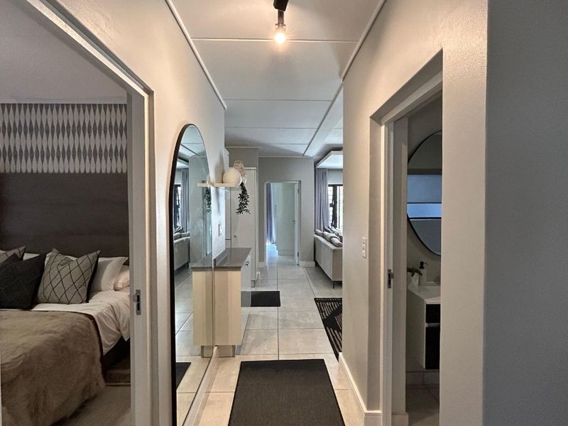 A well-lit hallway featuring tiled flooring and track lighting, providing access to the bedroom, bathroom, and living areas of the apartment.
