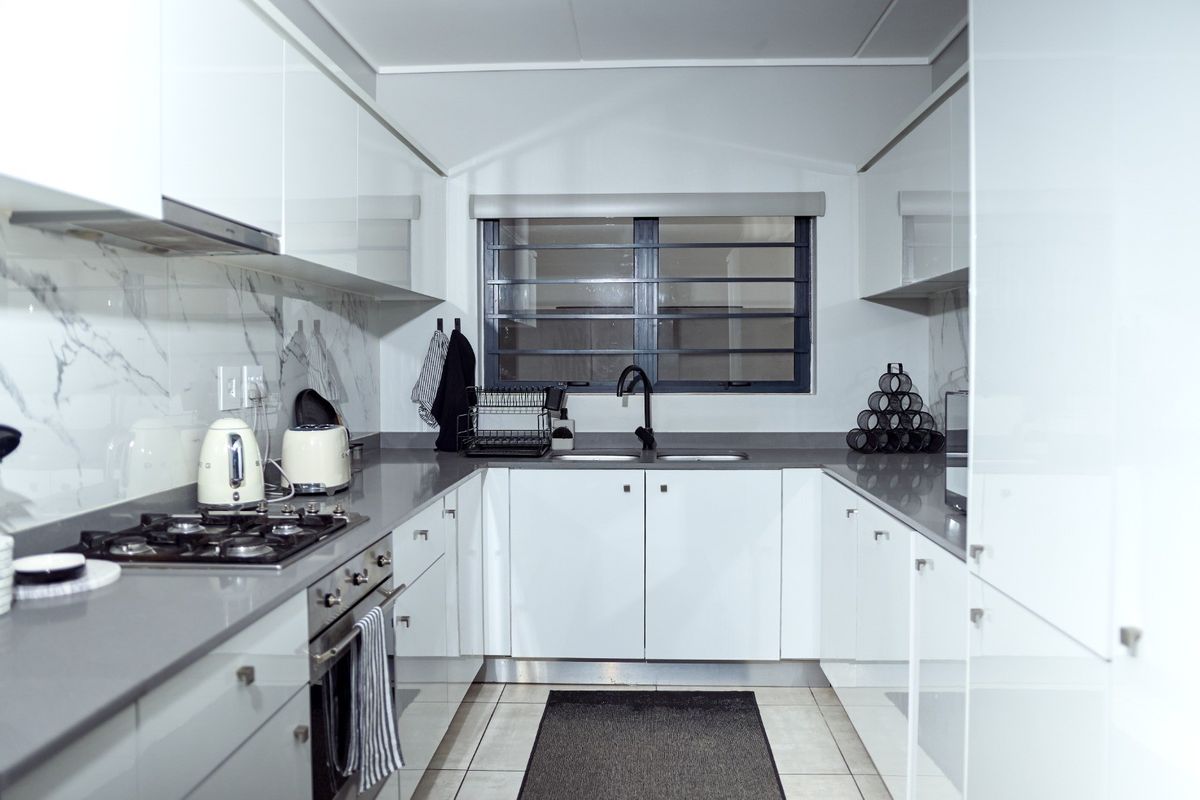 Modern galley kitchen featuring high-gloss white cabinetry, quartz countertops, marble-look splashback, gas hob, and integrated oven.