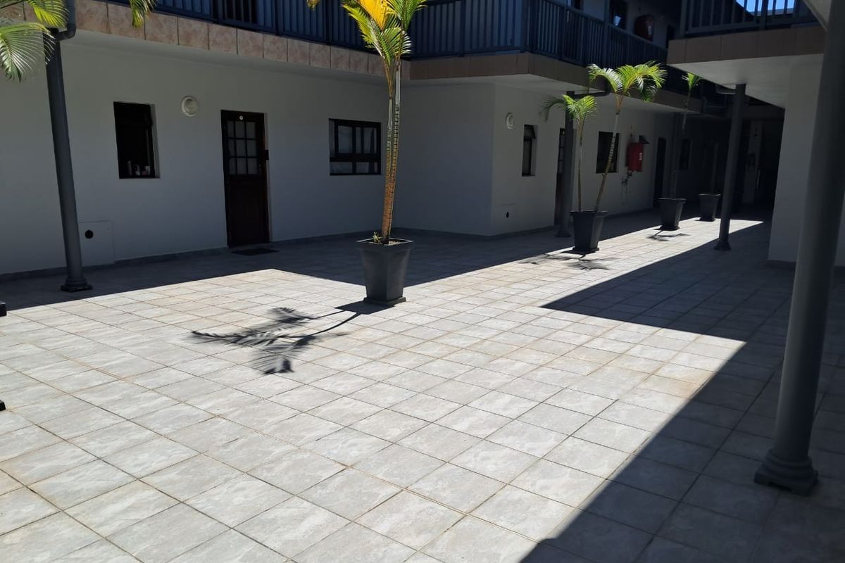 A paved courtyard area within an apartment complex, featuring tiled flooring, support columns, and access to upper-level balconies.