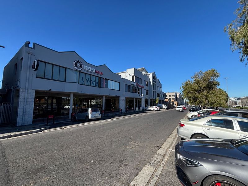 Street-level view of a commercial office building complex with storefronts and street parking.
