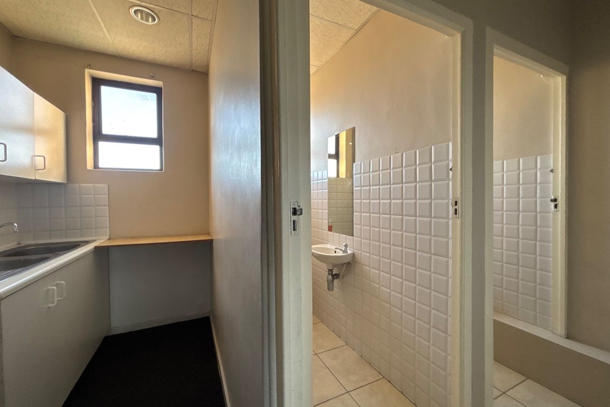 A functional office kitchenette area featuring built-in cabinetry, a sink, and adjacent tiled washroom facilities with wall-mounted basins.