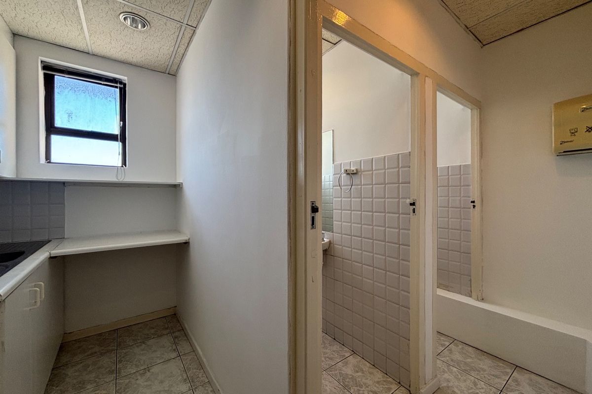A functional office bathroom facility featuring partitioned cubicles, tiled flooring, and built-in vanity counters with dated finishes.