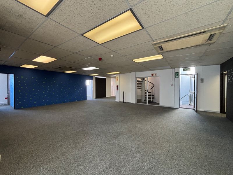 Spacious open-plan office area featuring a suspended ceiling, recessed lighting, ducted air conditioning, and a spiral staircase leading to an emergency exit.