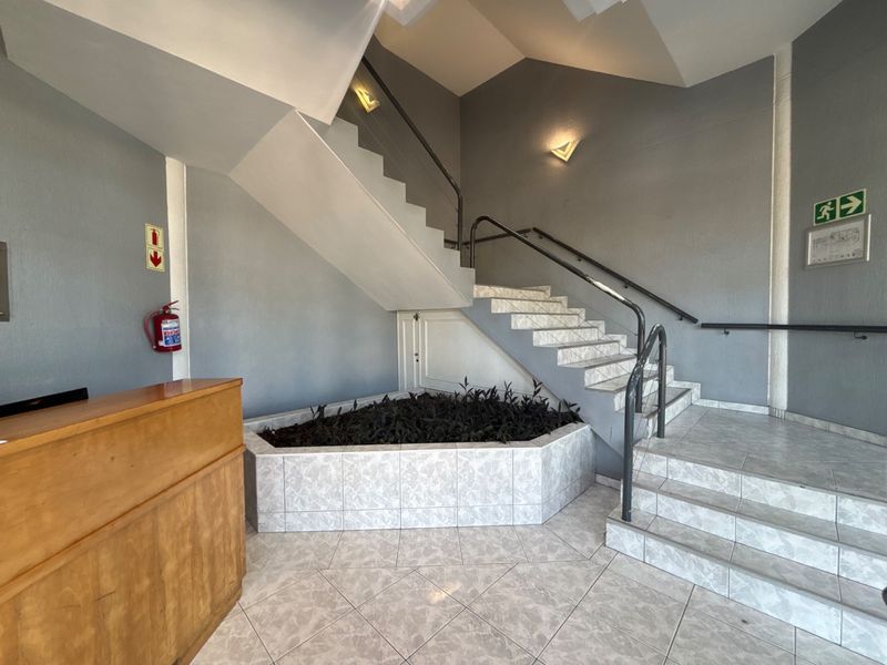 A bright office building entrance featuring a tiled staircase, metal handrails, and a built-in planter area under the stairs.