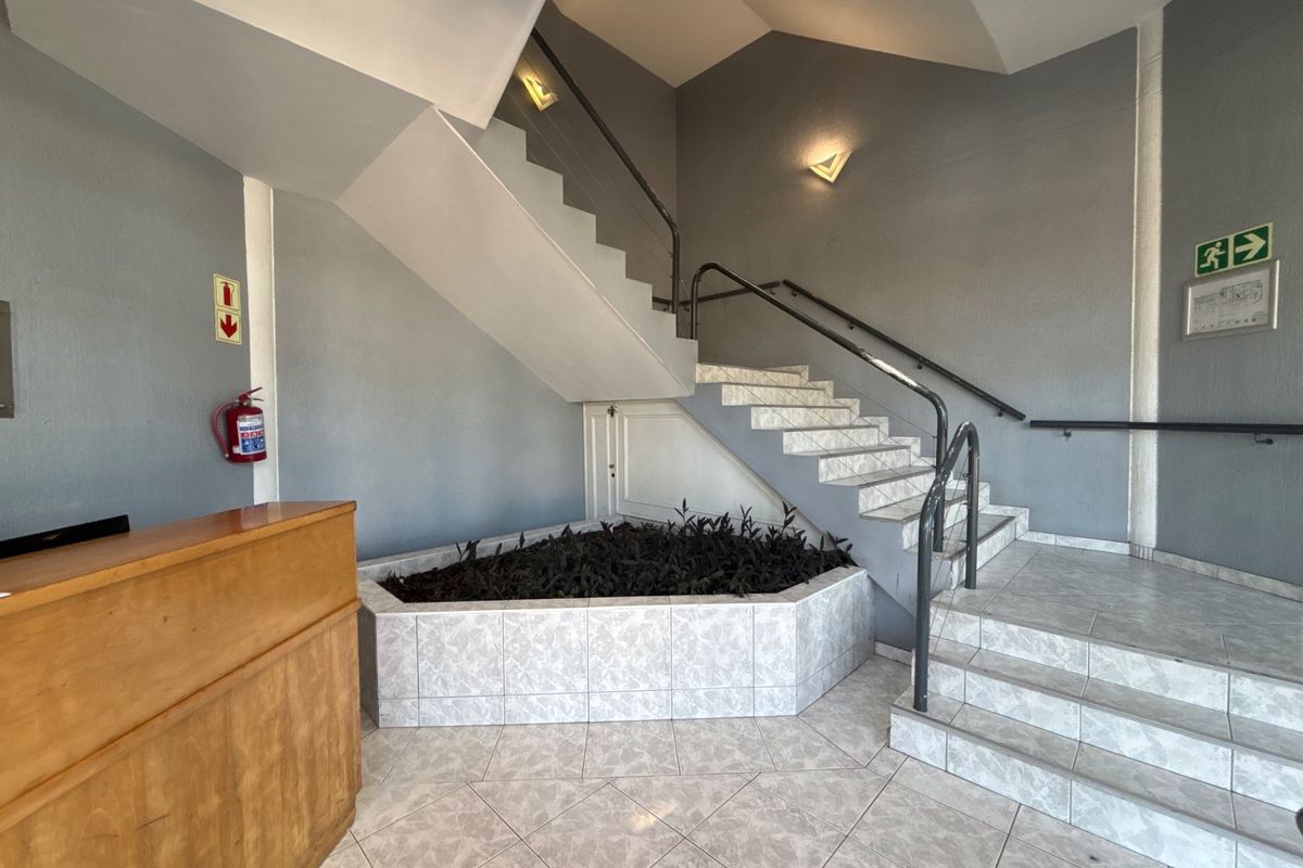 A bright office building entrance featuring a tiled staircase, metal handrails, and a built-in planter area under the stairs.