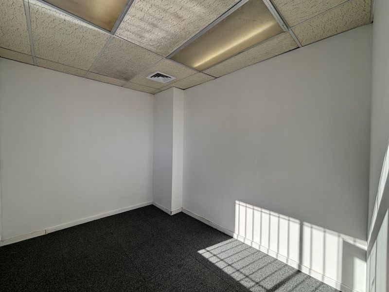 An empty office space featuring a suspended ceiling with recessed lighting, air conditioning vent, and dark carpeted flooring.
