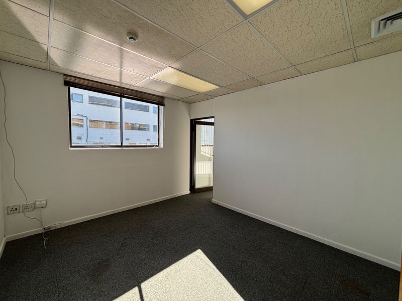 A vacant office space featuring carpeted flooring, a suspended ceiling with recessed lighting, and an air conditioning vent.