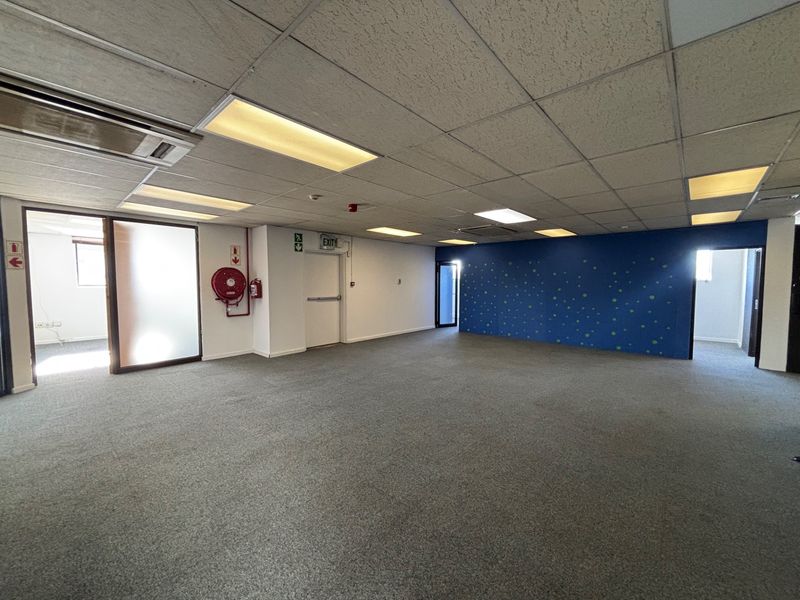 Spacious open-plan office area featuring suspended ceilings, recessed lighting, integrated air conditioning, and carpeted flooring with fire safety equipment installed.