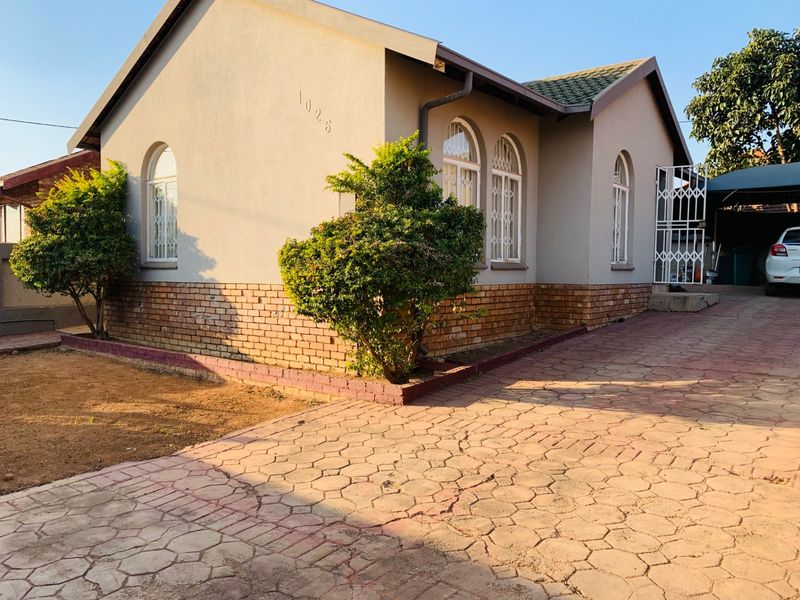 Front elevation of a single-story house featuring arched windows, brick base detailing, and a paved driveway.