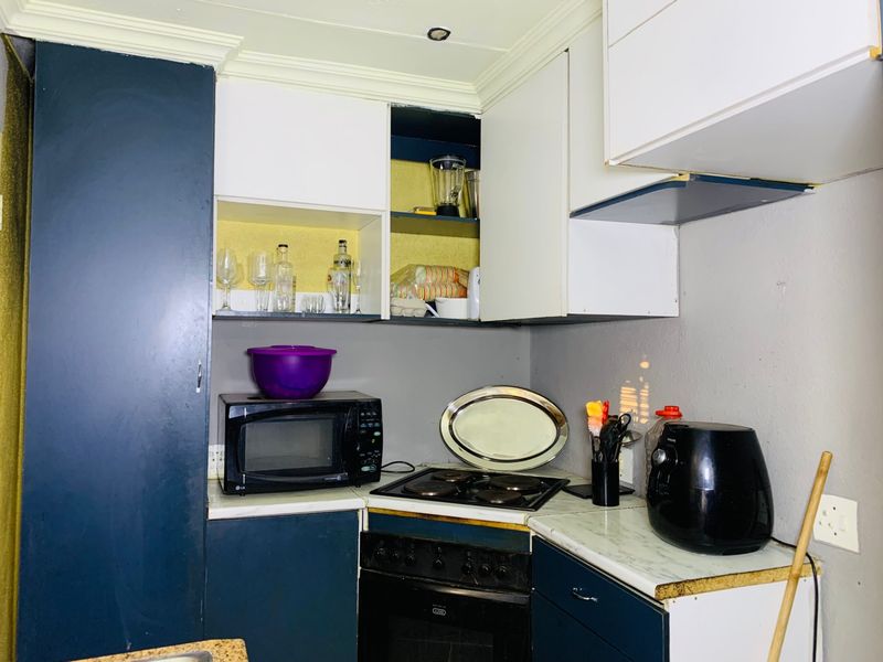 A compact kitchen featuring dark blue and white cabinetry, an electric hob, and an integrated oven, showing signs of wear and missing cabinet doors.