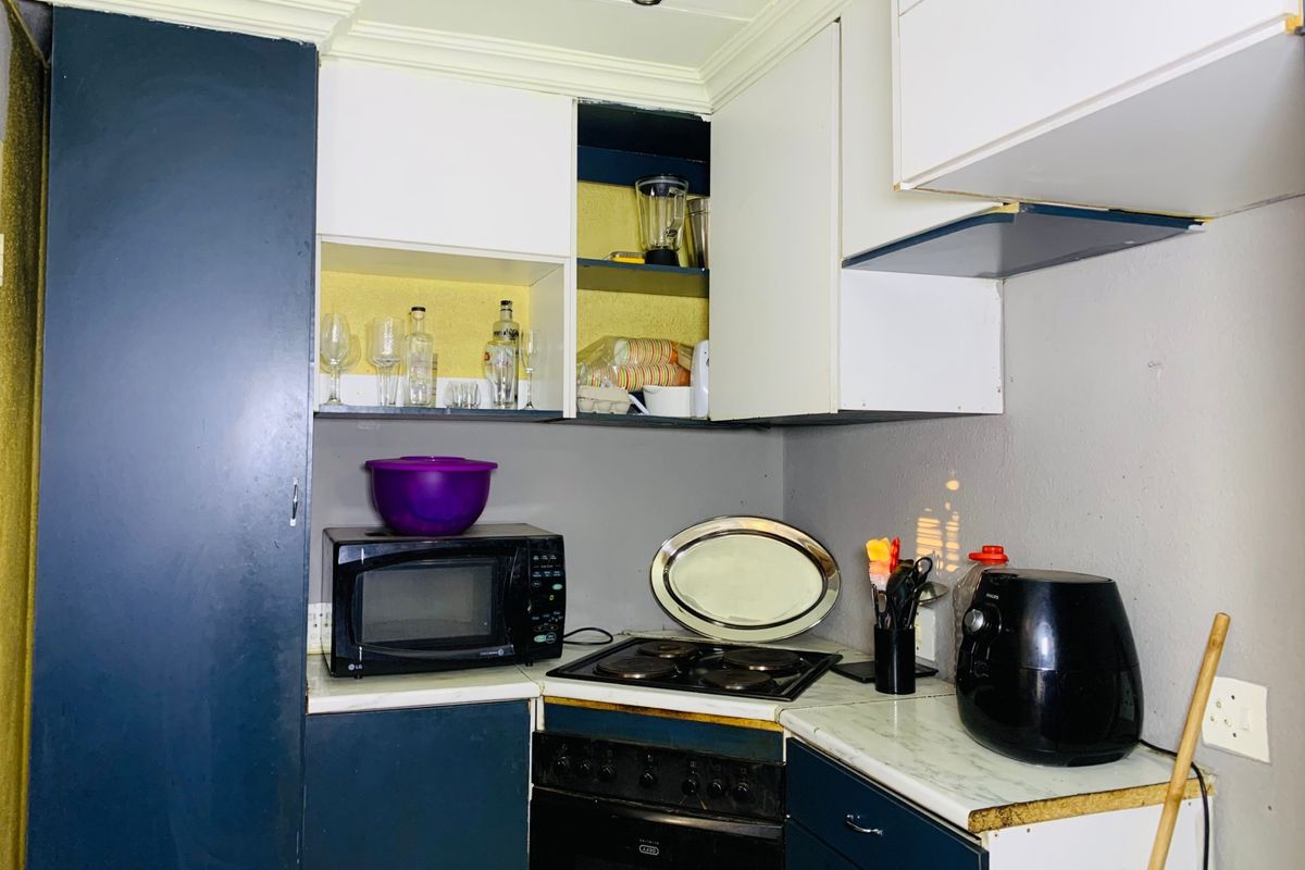A compact kitchen featuring dark blue and white cabinetry, an electric hob, and an integrated oven, showing signs of wear and missing cabinet doors.