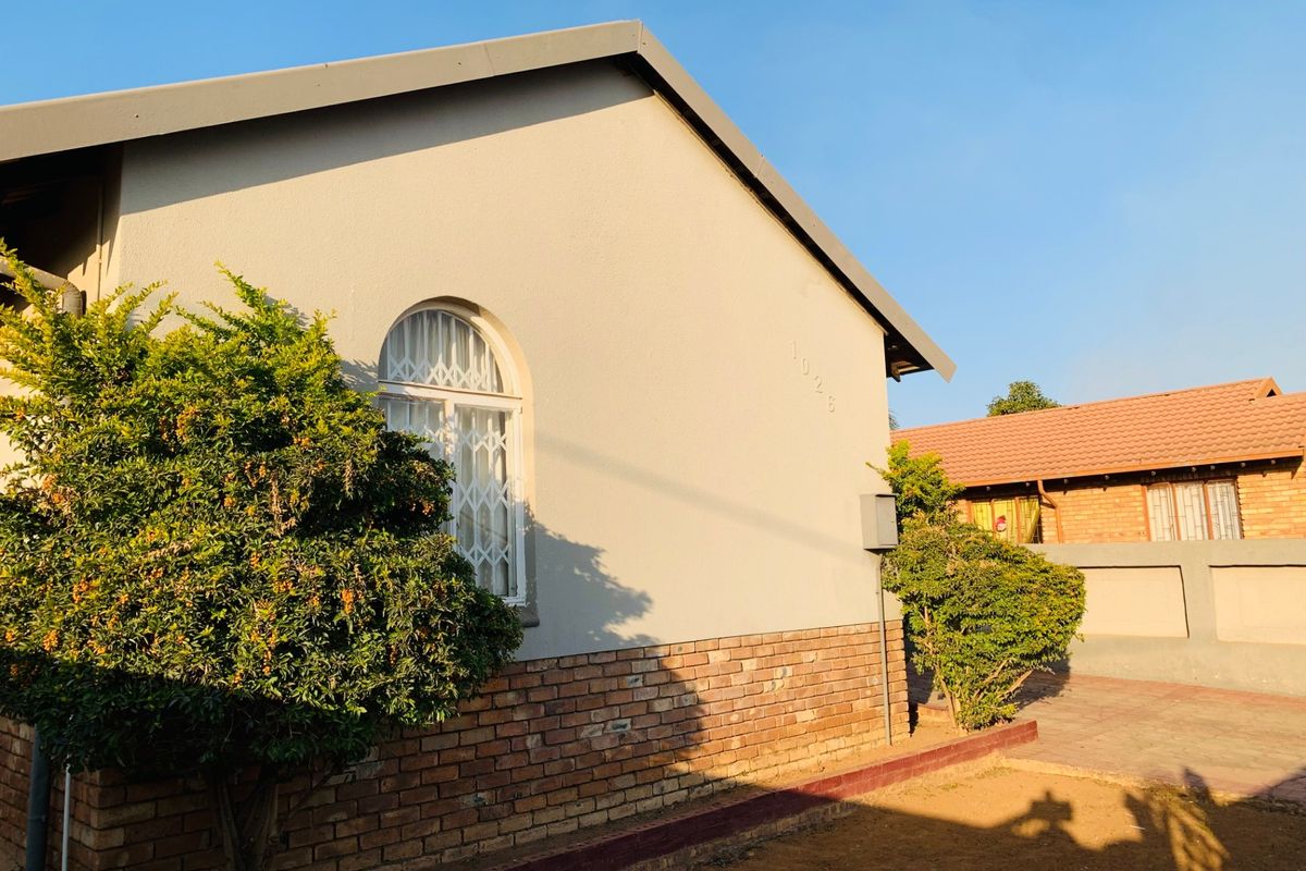 A view of the rear exterior facade featuring a brick plinth, plastered walls, and an arched window with security bars.