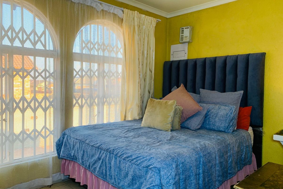 A bedroom featuring arched windows with security gates and a prominent blue upholstered headboard against a yellow wall.
