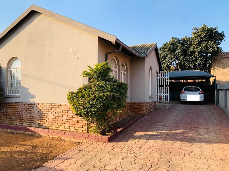 Front view of a single-story house featuring a brick facade, arched windows, and a paved driveway leading to a covered carport.