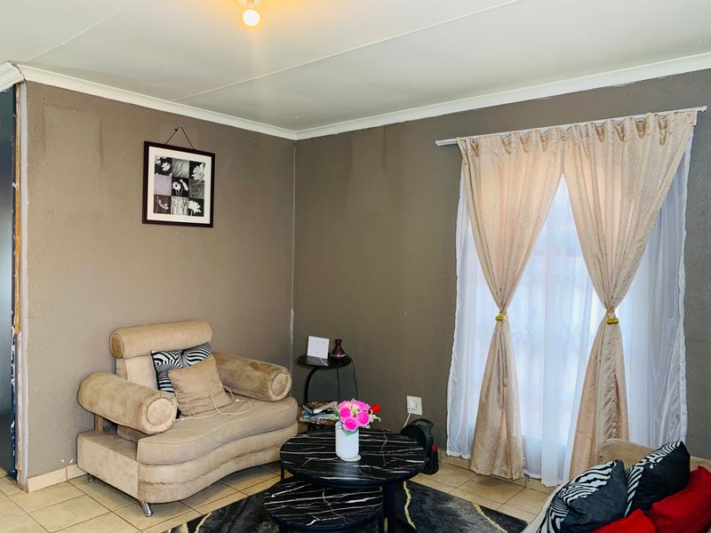 A living room area featuring tiled flooring and a window with curtain fixtures, showing signs of wear on the walls.