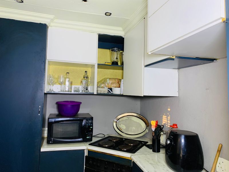 A compact kitchen area featuring built-in cabinetry, an electric hob, and an integrated oven, currently showing signs of wear and missing cabinet components.
