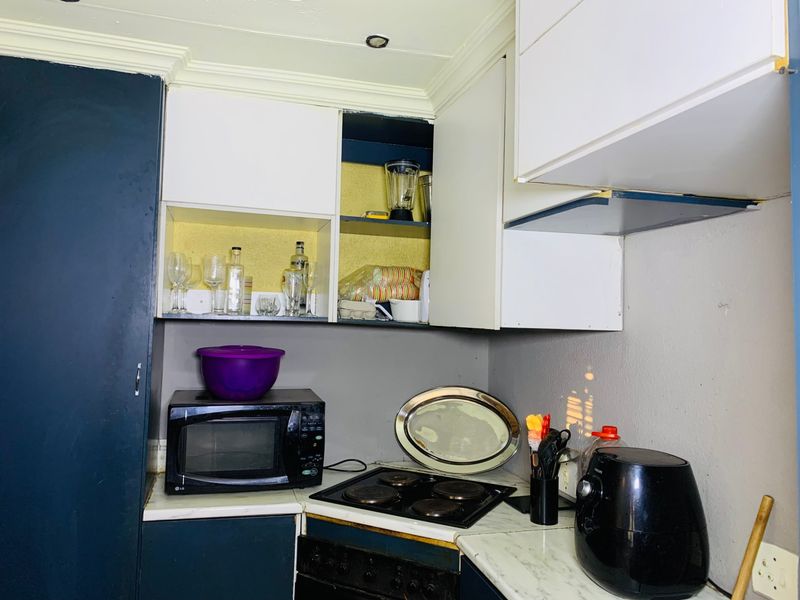 A compact kitchen area featuring built-in cabinetry, an electric hob, and laminate countertops, currently showing signs of wear and requiring cosmetic updates.