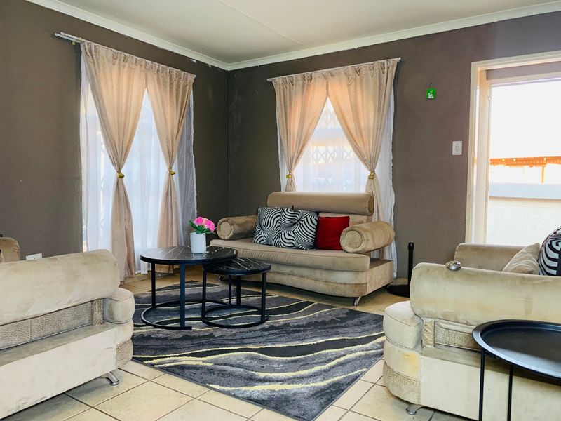 A living room featuring tiled flooring and dual windows with curtain rods, requiring minor cosmetic updates to the wall finishes.