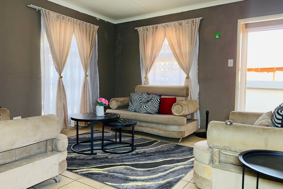 A living room featuring tiled flooring and dual windows with curtain rods, requiring minor cosmetic updates to the wall finishes.