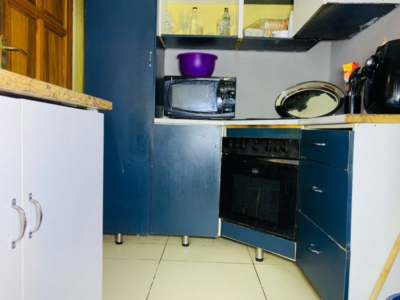 A compact kitchen featuring dark blue cabinetry, a built-in oven, and granite countertops, requiring cosmetic updates to improve its overall aesthetic and functionality.