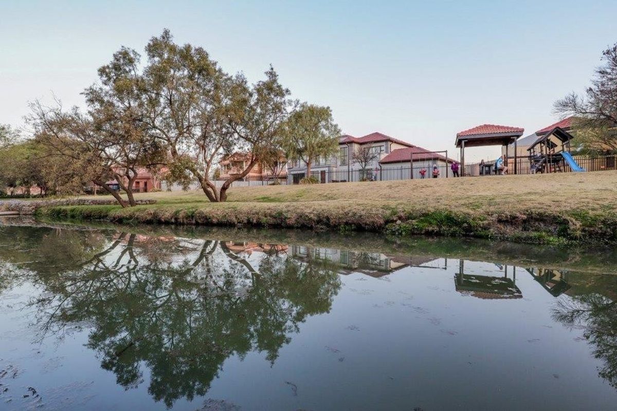 A scenic view of the rear property boundary featuring a landscaped lawn, mature trees, and metal perimeter fencing overlooking a tranquil water feature.