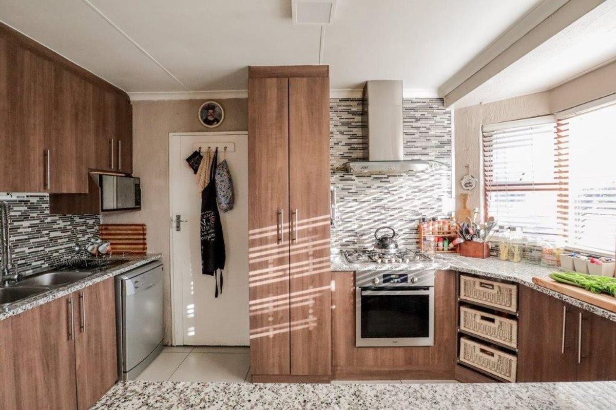 A functional kitchen featuring wood-finish cabinetry, granite countertops, a mosaic tile backsplash, and integrated stainless steel appliances including an oven and gas hob.