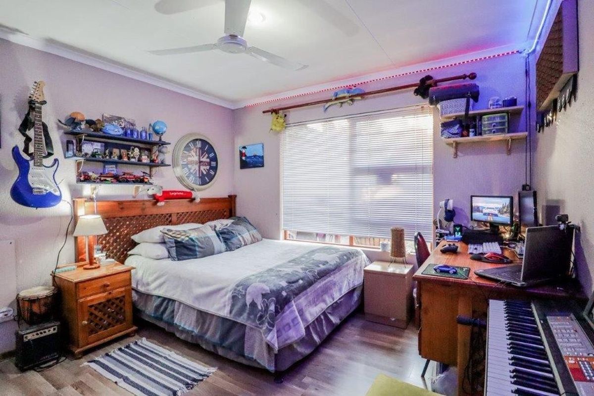 A bedroom featuring laminate flooring, a ceiling fan, and venetian blinds, currently utilized as a multi-purpose sleeping and workspace area.