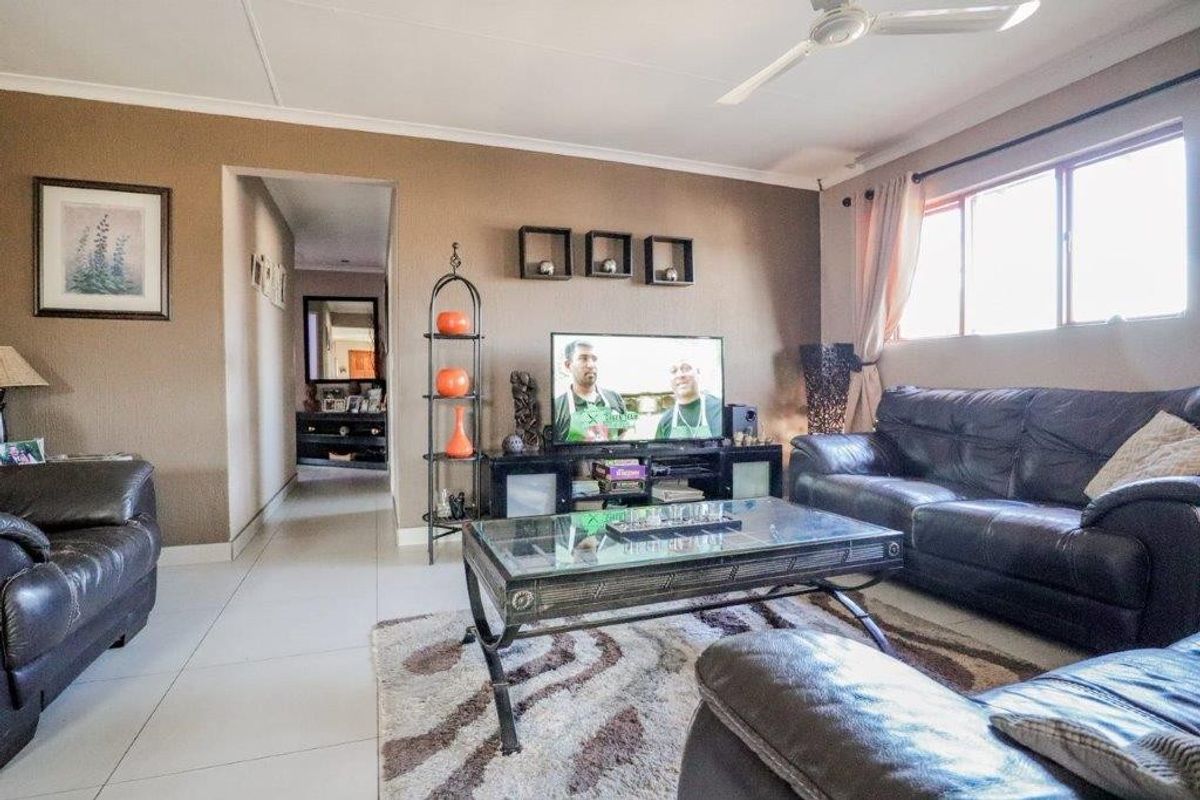 A comfortable living room featuring tiled flooring, a ceiling fan, and natural light from a large window, leading into a hallway.