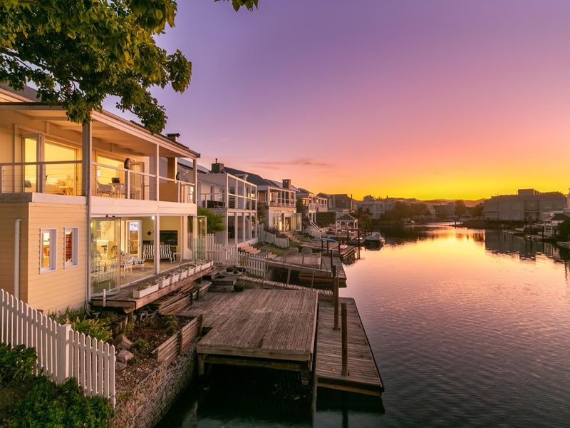 Waterfront property featuring a multi-level timber deck, private jetty, and balcony overlooking the canal at sunset.
