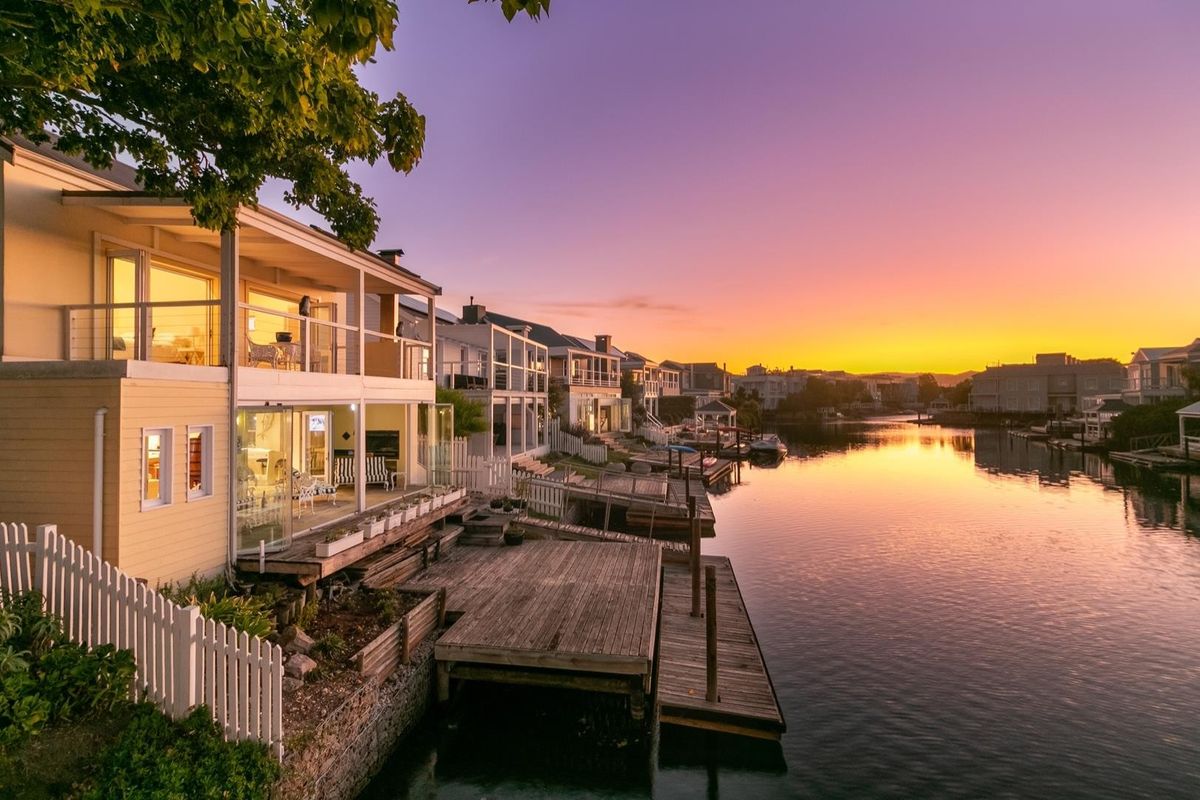 Waterfront property featuring a multi-level timber deck, private jetty, and balcony overlooking the canal at sunset.