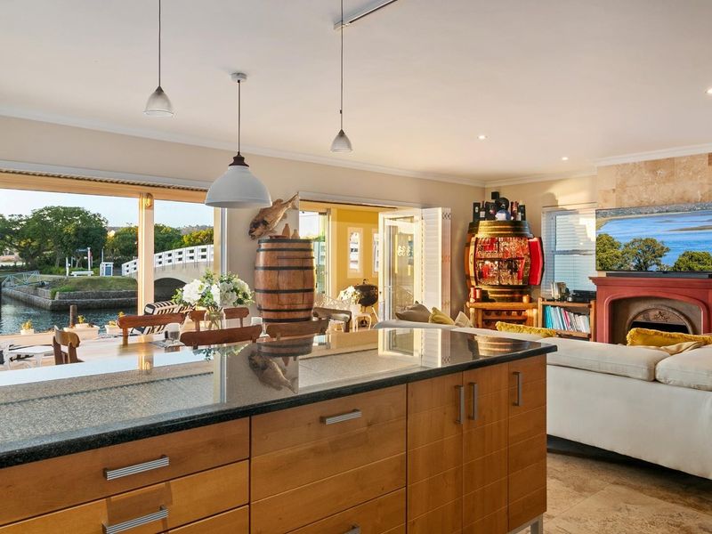 Spacious open-plan living area featuring a modern kitchen island, stone fireplace, and large sliding doors opening to a scenic waterfront patio.