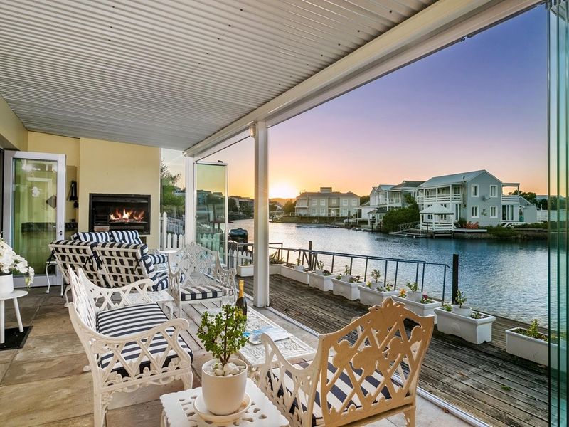 Covered patio featuring a built-in fireplace, timber decking, and glass stacker doors, offering scenic waterfront views.