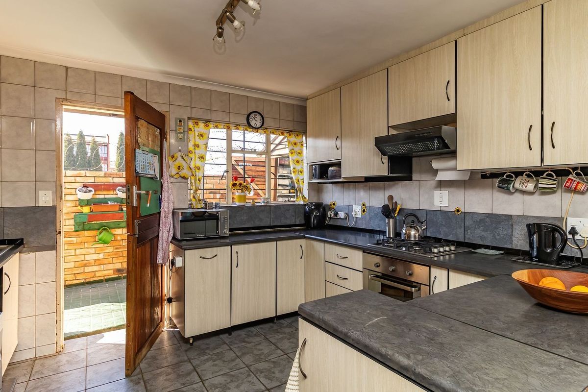 Functional kitchen featuring light wood-finish cabinetry, dark laminate countertops, built-in oven with gas hob, and direct access to an outdoor area.