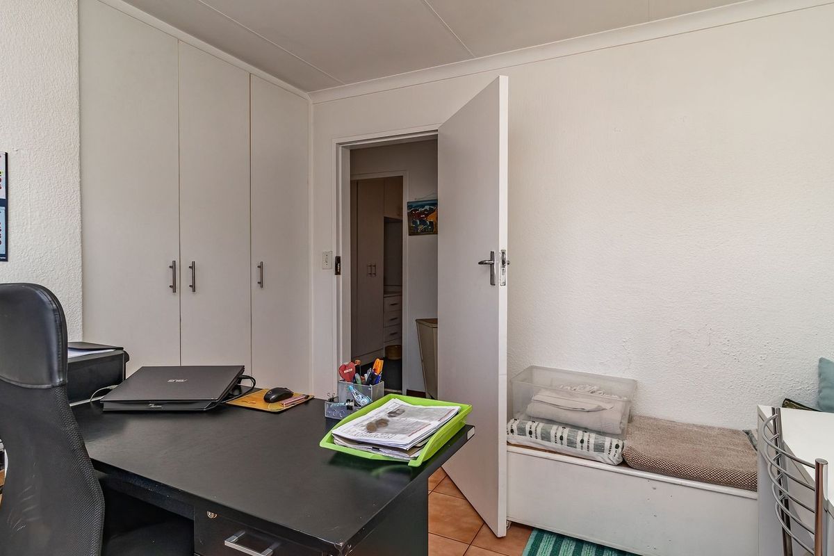 A bedroom featuring built-in cupboards and tiled flooring, currently utilized as a home office space.