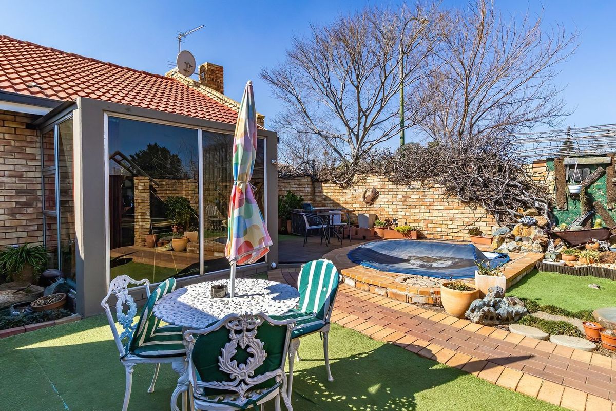 Rear garden area featuring a small built-in pool, brick paving, artificial lawn, and a covered patio section with sliding glass doors.