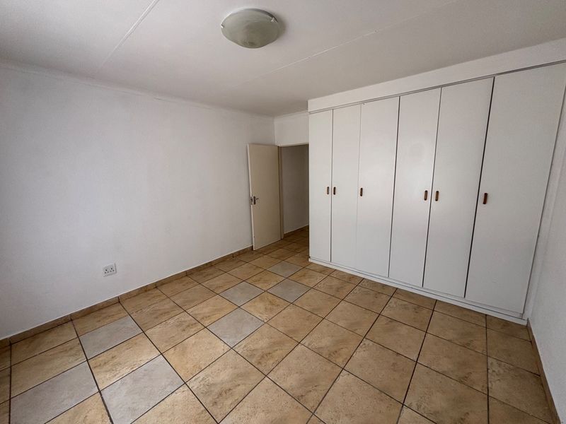 A clean, empty bedroom featuring neutral tiled flooring and ample built-in cupboard storage space.