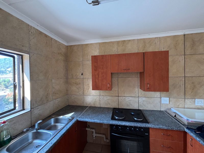 A functional kitchen featuring granite countertops, a double bowl sink, built-in oven, electric hob, and tiled splashback, with some cabinetry maintenance required.