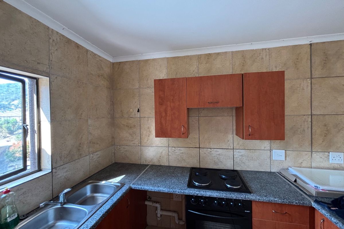 A functional kitchen featuring granite countertops, a double bowl sink, built-in oven, electric hob, and tiled splashback, with some cabinetry maintenance required.