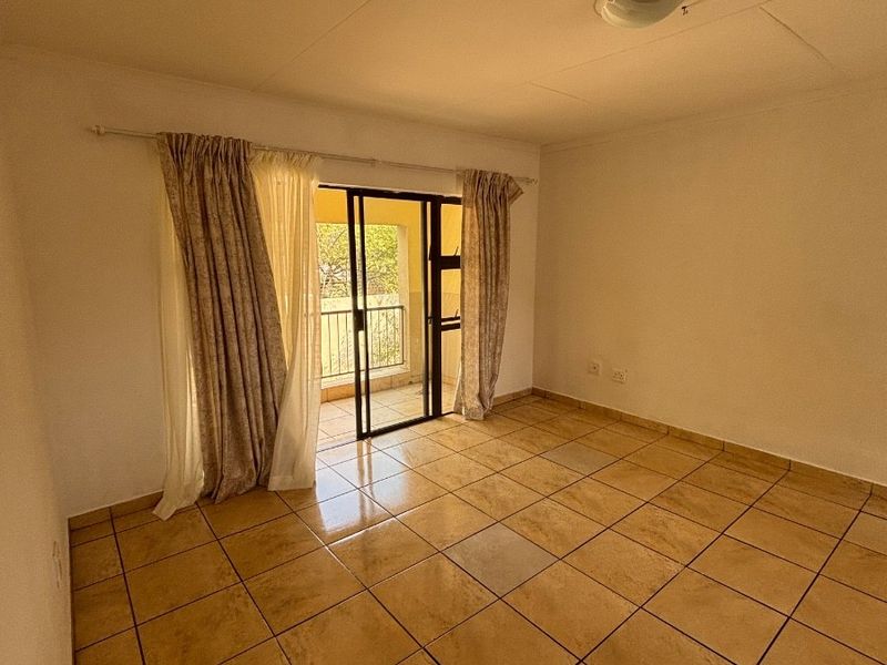 An empty living room featuring tiled flooring and a sliding glass door providing access to an outdoor balcony area.