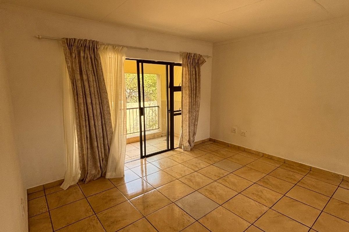 An empty living room featuring tiled flooring and a sliding glass door providing access to an outdoor balcony area.