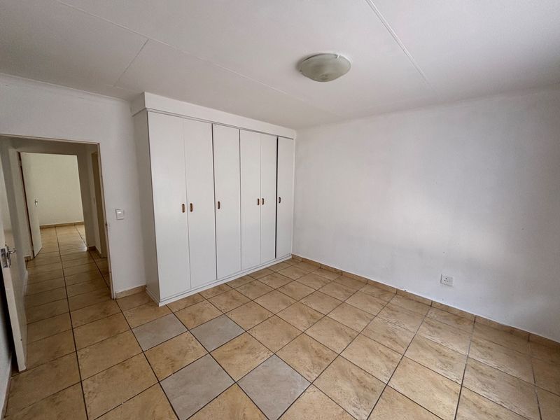 A bright, empty bedroom featuring neutral tiled flooring and ample built-in cupboard storage, offering a clean canvas for personalization.
