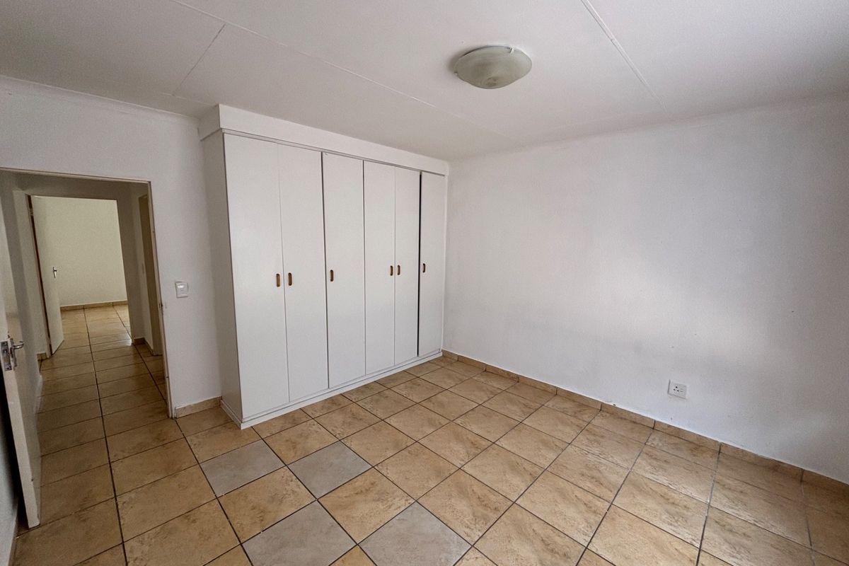 A bright, empty bedroom featuring neutral tiled flooring and ample built-in cupboard storage, offering a clean canvas for personalization.