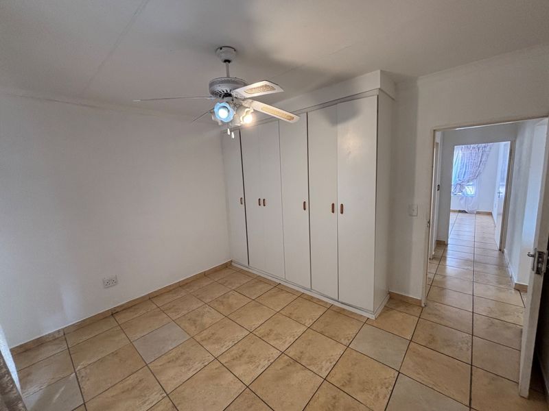 A bright, empty bedroom featuring built-in cupboards, a ceiling fan, and neutral tiled flooring, offering a clean canvas for personalization.