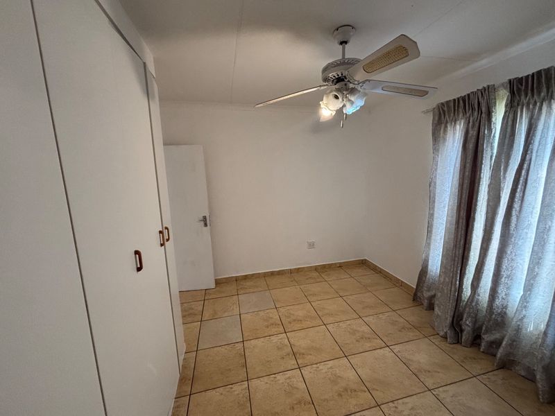 A vacant bedroom featuring built-in cupboards, a ceiling fan, and tiled flooring, offering a neutral space ready for personalization.