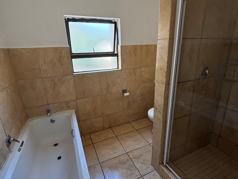 A functional bathroom featuring a bathtub, separate shower enclosure, and tiled finishes. The space is clean but dated, offering potential for modern renovation.