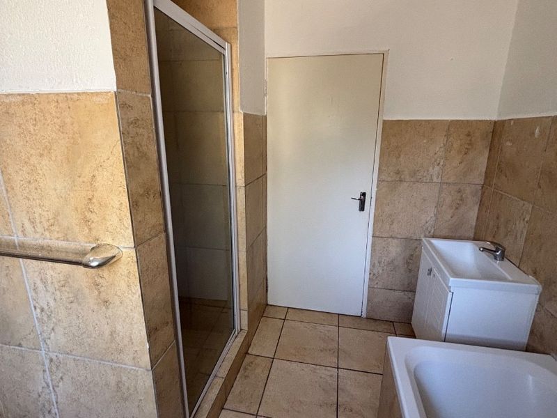 A functional bathroom featuring a shower enclosure, bathtub, and vanity basin with neutral tiled finishes throughout.