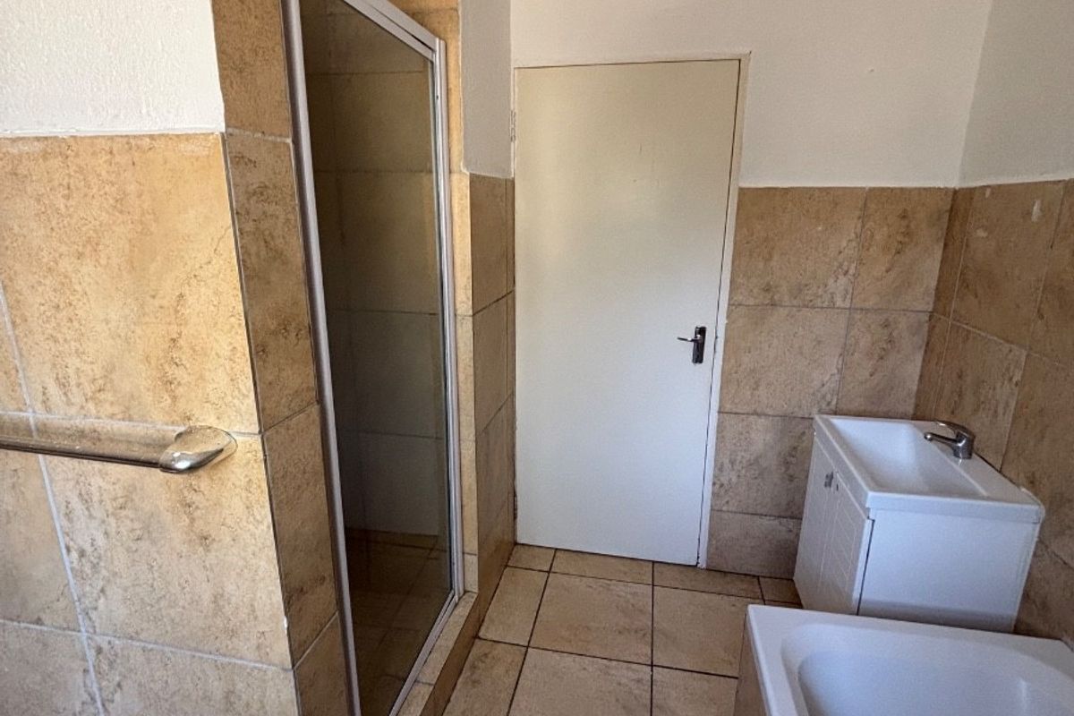 A functional bathroom featuring a shower enclosure, bathtub, and vanity basin with neutral tiled finishes throughout.