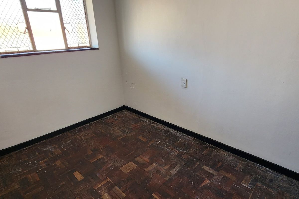 An empty bedroom featuring original parquet flooring and a window with security bars, requiring cosmetic updates to the walls and flooring.